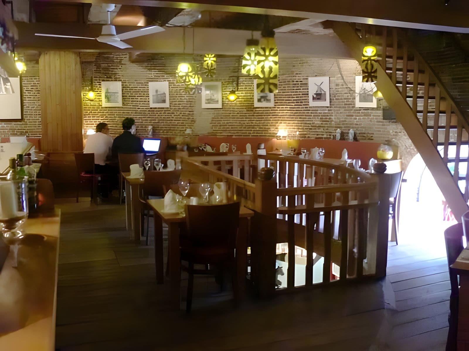 Warm verlichte eetzaal van De Noordmolen, met foto's van molens aan de bakstenen muur en een houten trap naar de bovenverdieping