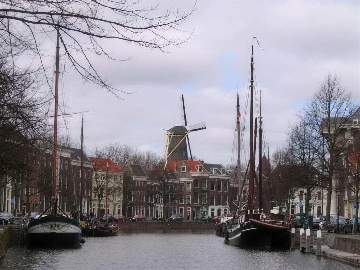 Uitzicht over een Schiedamse gracht met traditionele zeilschepen en de Noordmolen op de achtergrond